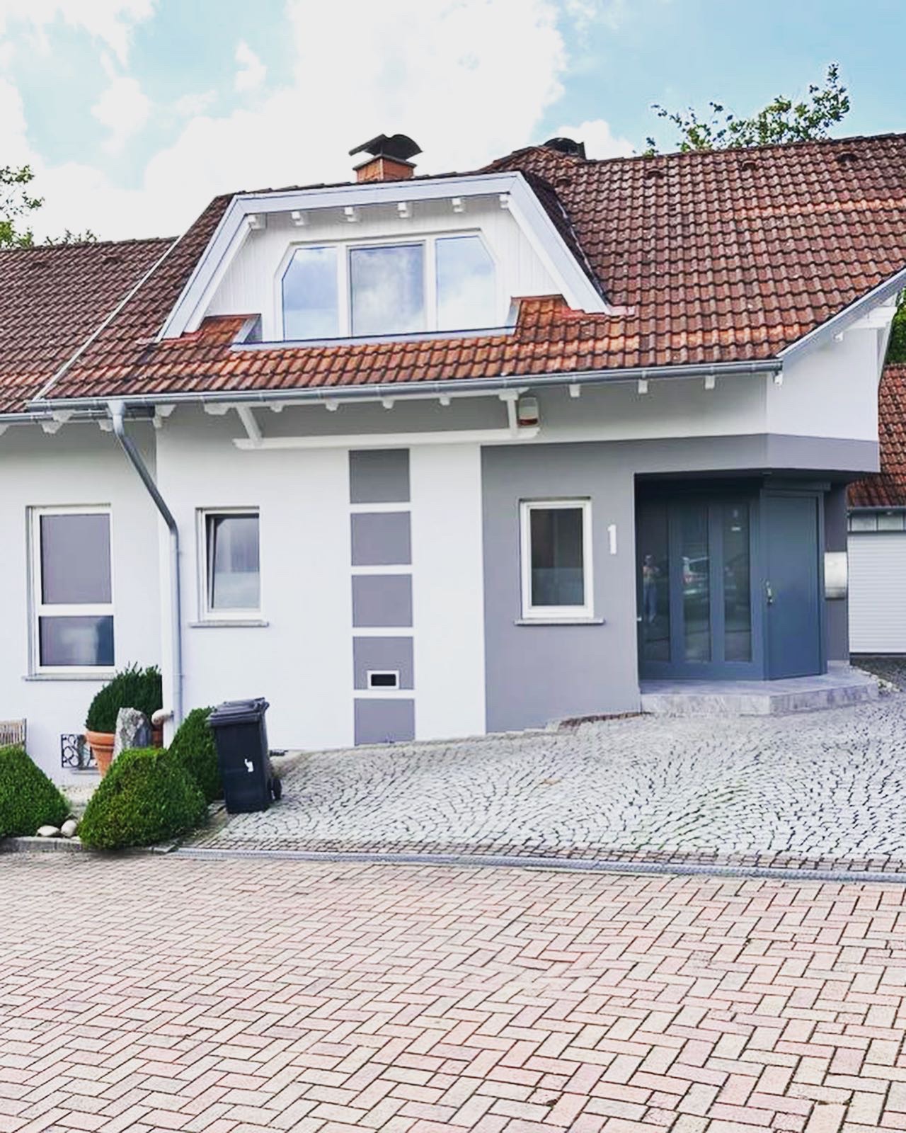 Küche mit Esstisch, Stühlen und bunter Tischdecke. Im Hintergrund begrünte Mauer und Geländer, das an einen Wasserbereich grenzt. Schattenwurf und Bepflanzung am Rand.