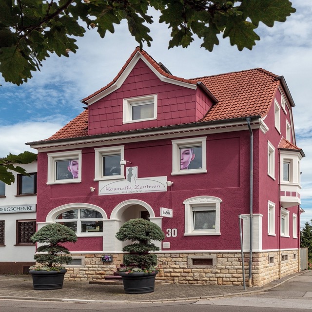 Zweistöckiges Wohnhaus mit orangefarbener Fassade, Vorgarten und Eingangstreppe unter blauem Himmel.