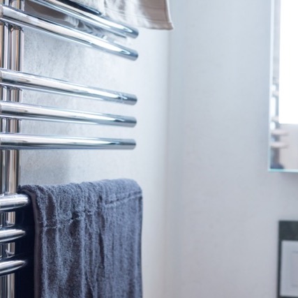 Ein Badezimmerdetail mit einem verchromten Handtuchhalter, auf dem ein graues Handtuch hängt, neben einer weißen Wand.