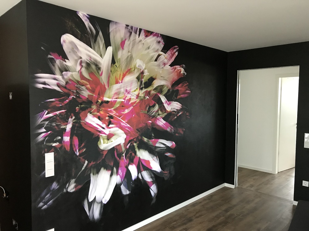 Schwarze Wand mit großem bunten Blumen-Kunstwerk, Holzboden und Tür im Hintergrund.