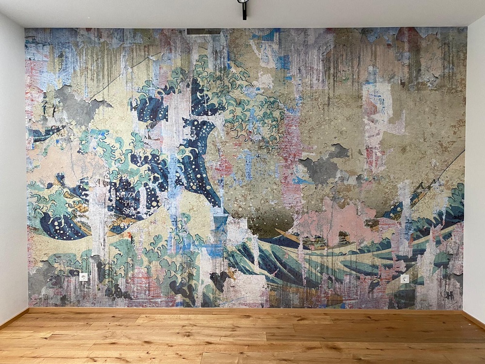 Wanddekoration mit grau-buntem Druck einer brausenden Welle. Der Fußboden ist aus Holzdielen.